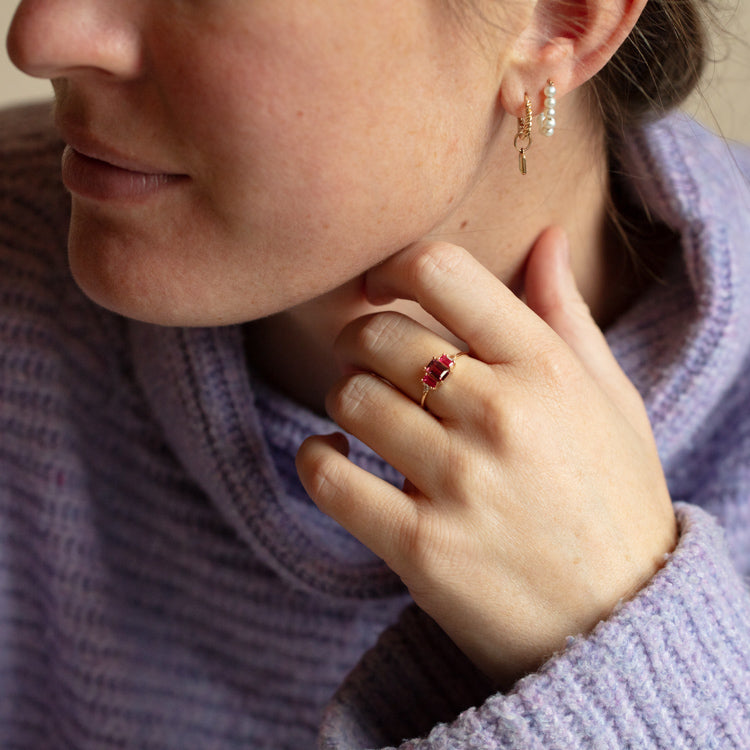 A woman in a purple sweater rests her chin on her hand, showcasing the 14kt Gold Rhodolite Garnet and Topaz Cascading Love Ring (sample size 7), with her partially visible face drawing attention to the elegant jewelry.