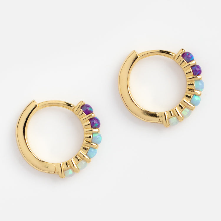 The Mini Opal Ombre Huggies are 18k yellow gold vermeil hoops with alternating purple and turquoise gemstones set along part of each hoop, shown on a white background.