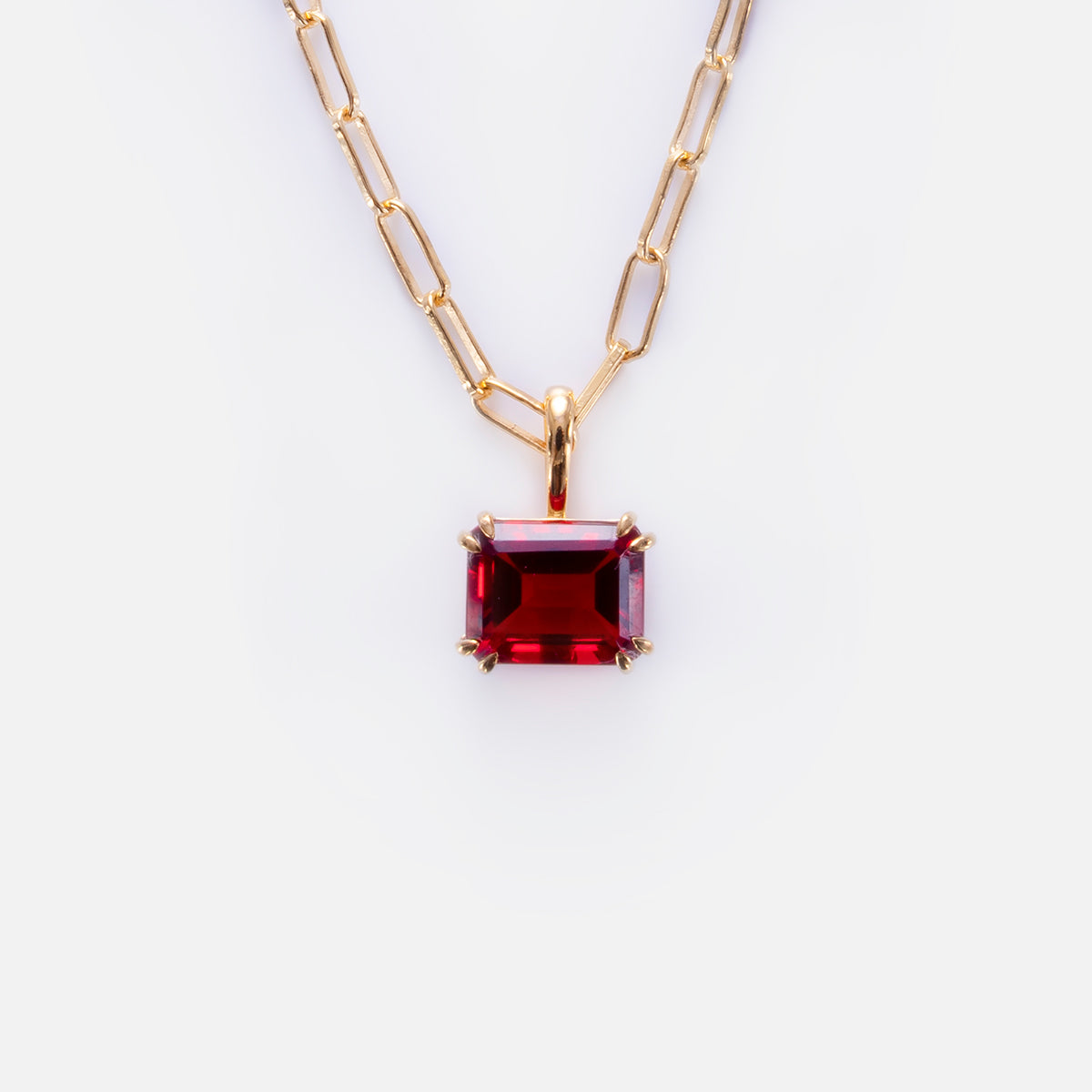 The Born to Shine Birthstone Necklace is a gold paperclip chain with a rectangular deep red gemstone pendant in a gold prong setting, shown on a white background.