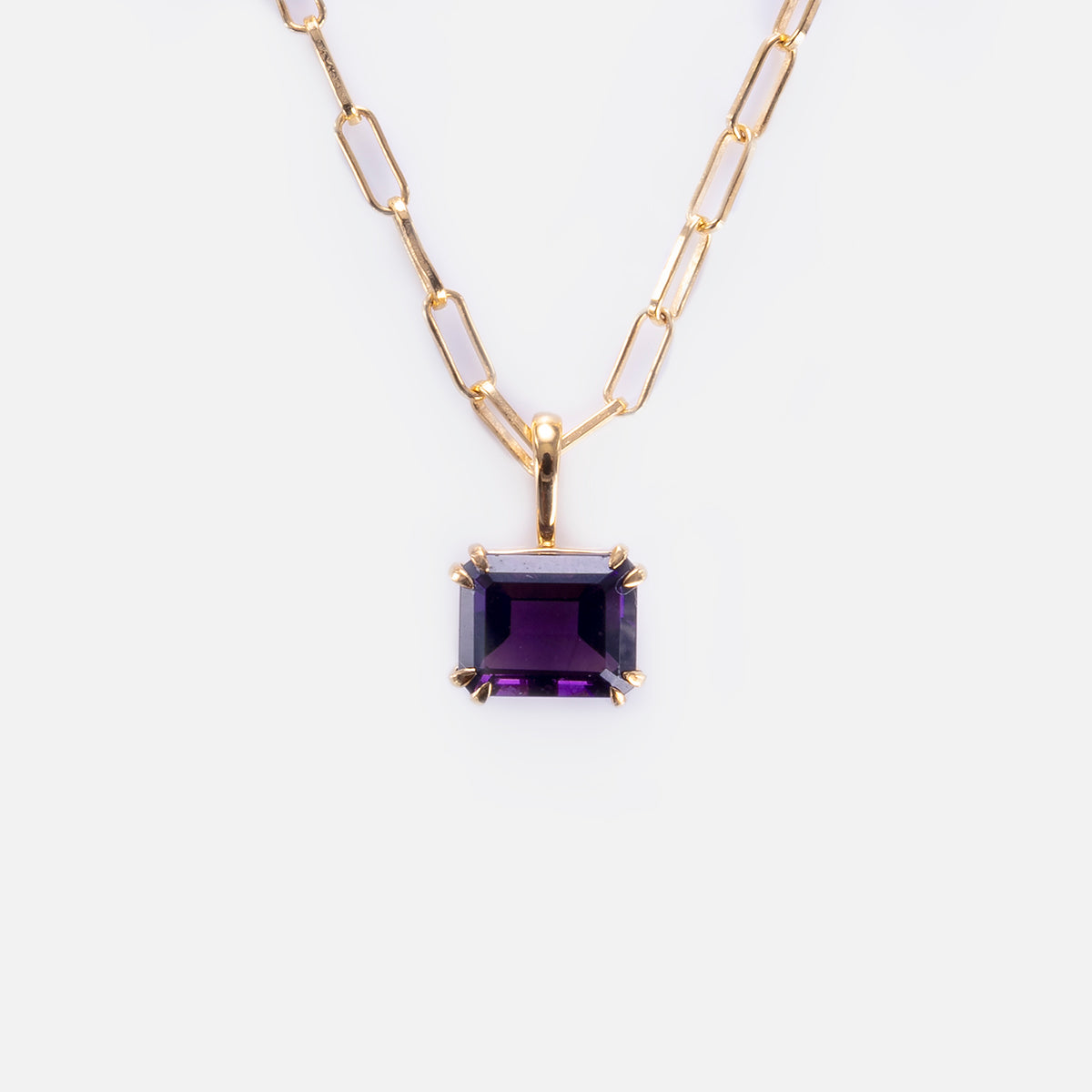 The Born to Shine Birthstone Necklace features a gold paperclip chain and a rectangular, faceted deep purple gemstone pendant in a gold prong setting, displayed against a plain white background.