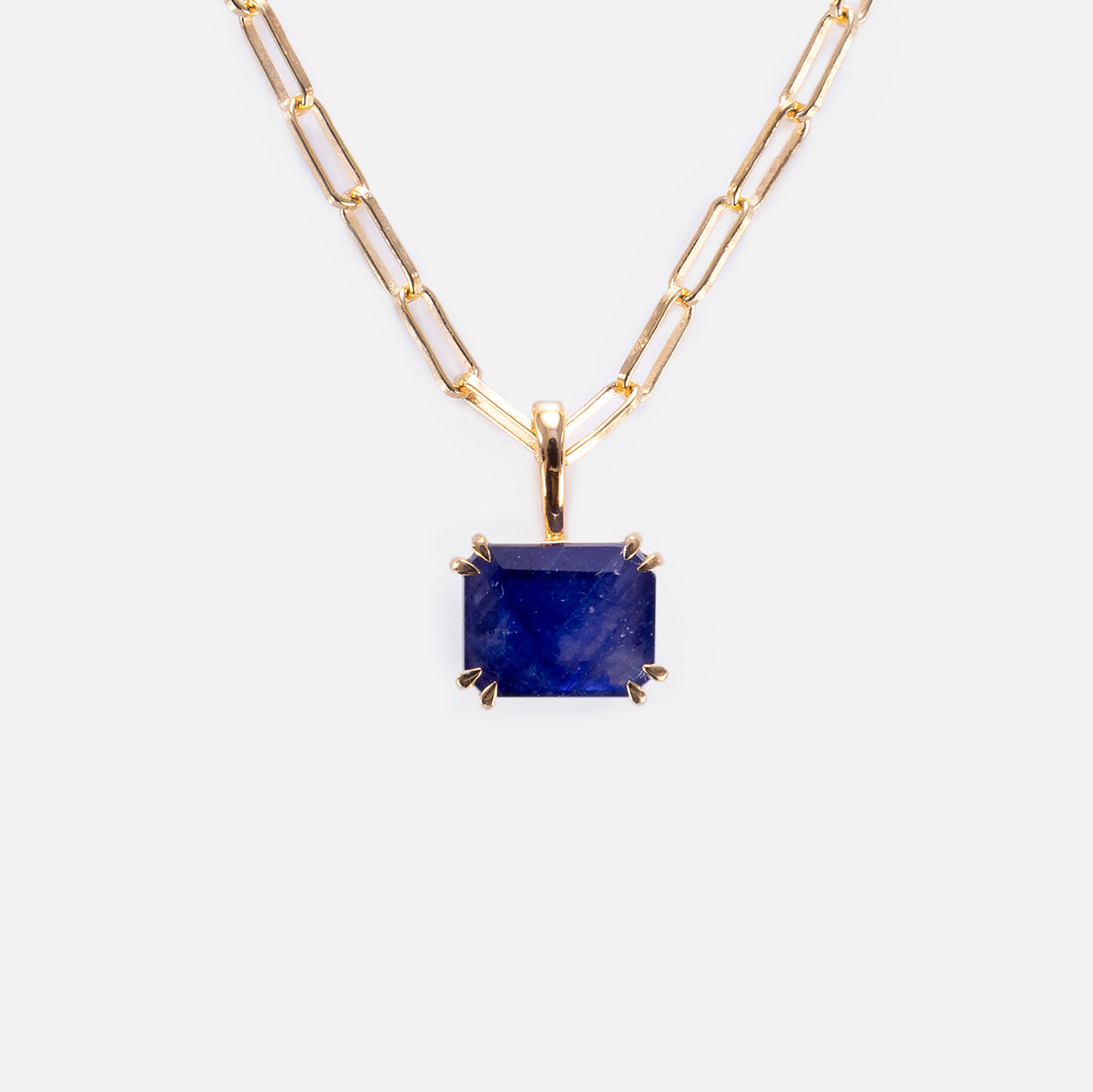 The Born to Shine Birthstone Necklace features a gold paperclip chain and a rectangular deep blue gemstone pendant in a four-prong gold setting, elegantly displayed on a plain white background.