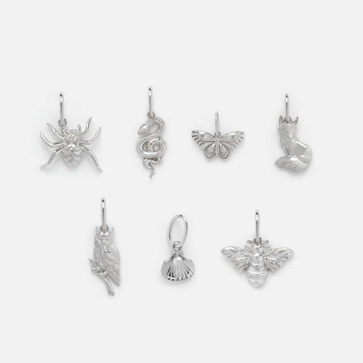 Seven silver charms, including a butterfly and bee, are displayed on a plain background in two neat rows. Each nature-inspired charm pairs beautifully with the Solid Gold Nature Charm in White Gold for added elegance.