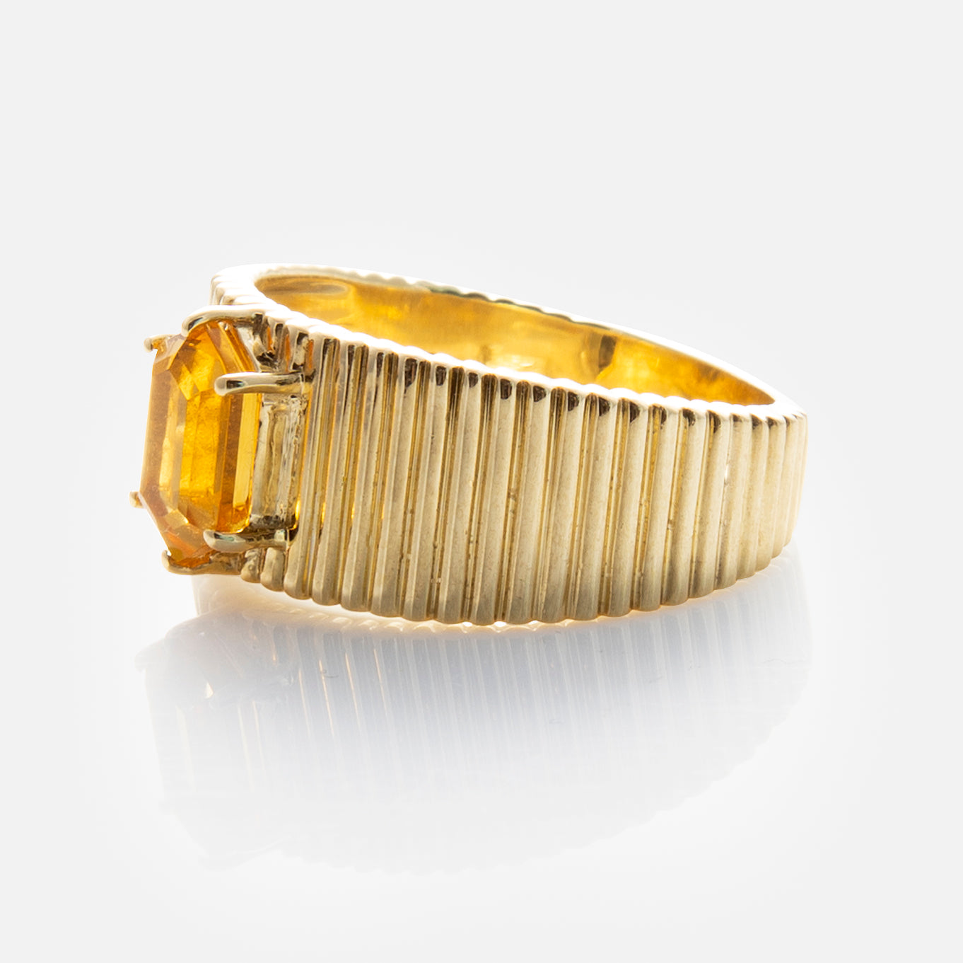 The Solid Gold Citrine Bold Fluted Cigar Band is a 9k yellow gold ring with a ridged band and rectangular yellow citrine in a prong setting, shown against a white background.