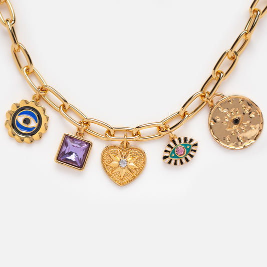 The San Miguel Necklace is a gold plated piece with five enamel glass charms: a blue and gold gear, purple square gemstone, gold heart with clear stone, striped eye charm, and an engraved medallion.