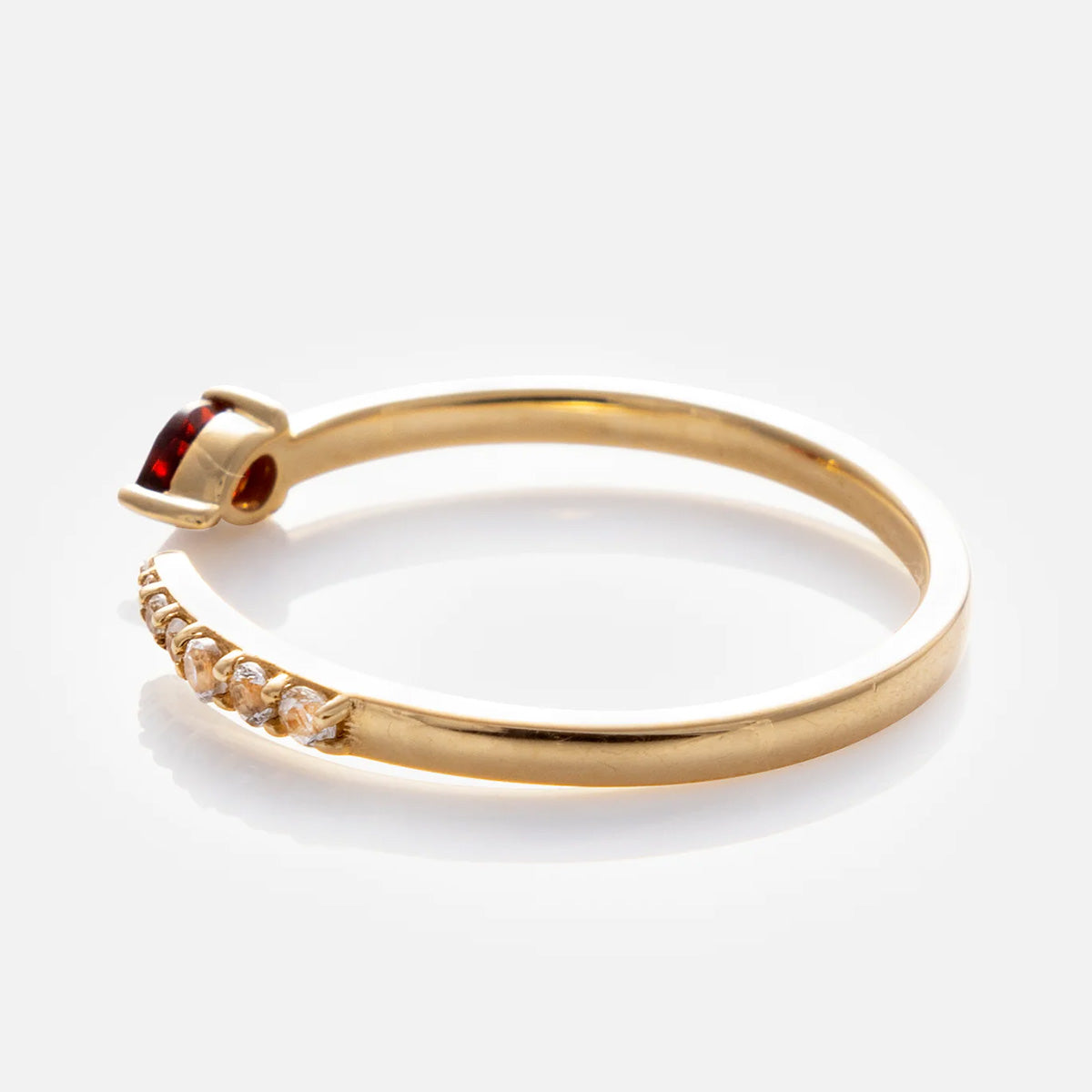 The Solid Gold Garnet and Sapphire Open Front Band in 9k yellow gold features a single red garnet in a prong setting, accented by sparkling sapphires along one side of the open band, shown on a white background.