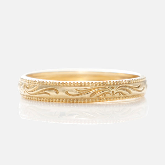 The Solid Gold Filigree Ring features intricate engraving and a beaded edge, showcased on a white reflective surface with a light background.