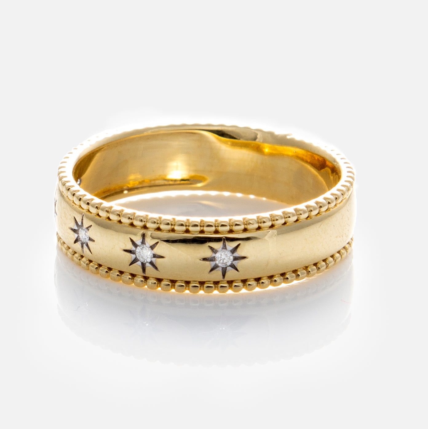 The Solid Gold Bold Star Set Diamond Band features five diamond-like stones in star-shaped settings spaced around a beaded gold band, displayed on a reflective white surface.