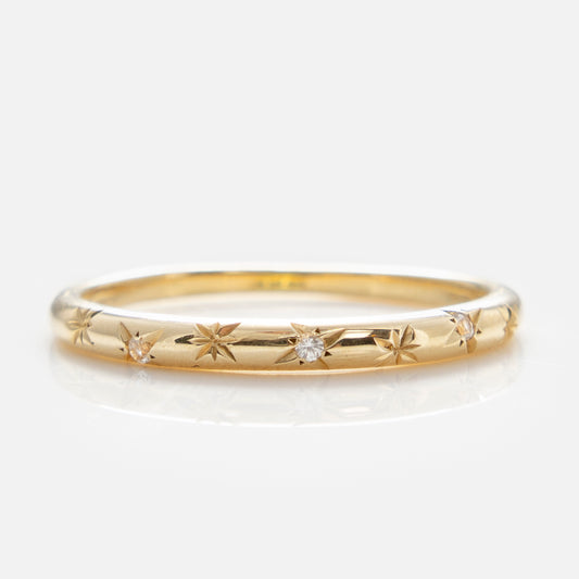 The Solid Gold Starry White Sapphire Band is a delicate everyday ring with thin solid gold, star-shaped engravings, and sparkling white sapphires at the center, elegantly displayed on a white background.