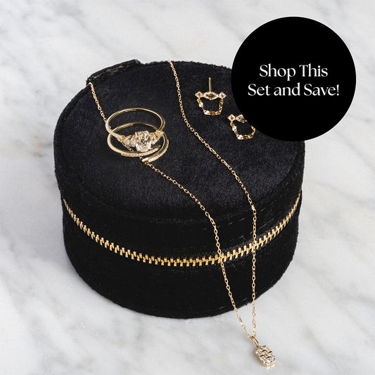 The Solid Gold 2025 April Capsule White Topaz Full Set, including a ring, necklace, and earrings, is displayed in a black velvet case with gold zipper. Shop This Set and Save! overlays the image on a white marble background. Free gift included.