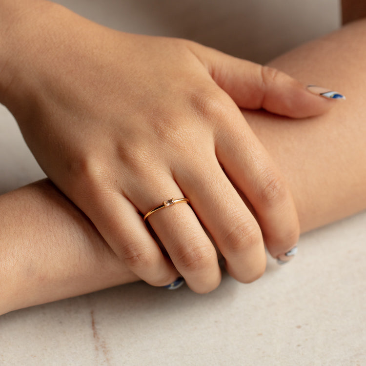 A hand with manicured nails rests on an arm, showcasing the Baguette Stacking Ring—crafted in 18k gold vermeil and featuring a small cubic zirconia stone—worn on the ring finger against a light, neutral background.