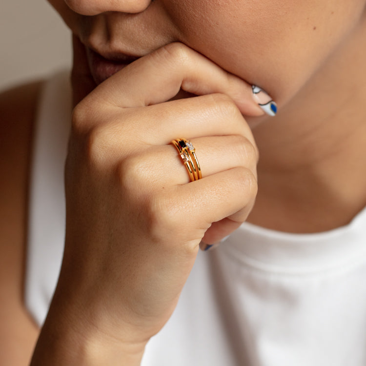 A person in a white sleeveless top rests their chin on their hand, highlighting the Baguette Stacking Ring. Their nails feature a white and blue manicure.