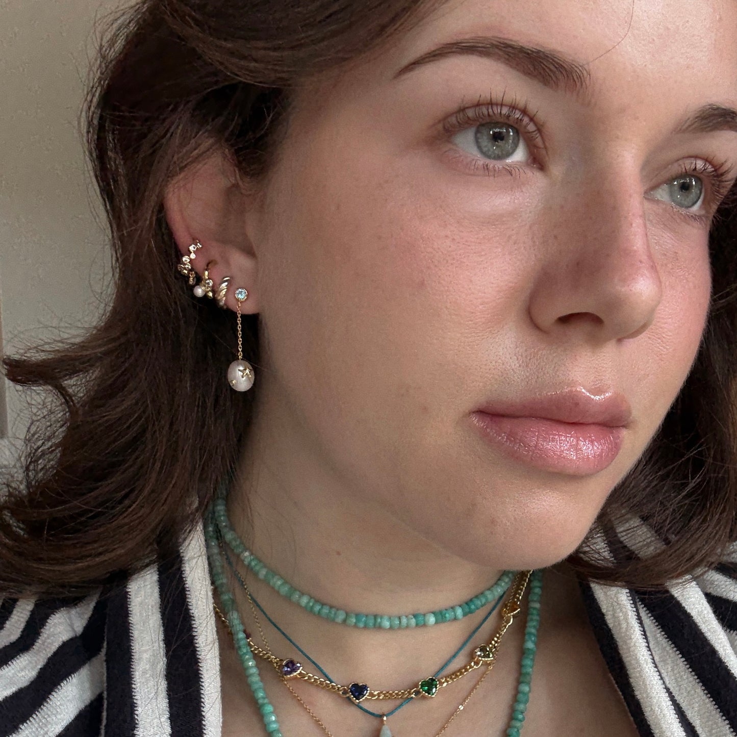 A woman with light eyes and brown hair wears layered turquoise and gold necklaces and multiple Gem Accent Pearl Drop Earrings. She gazes slightly upward, dressed in a black and white striped top.