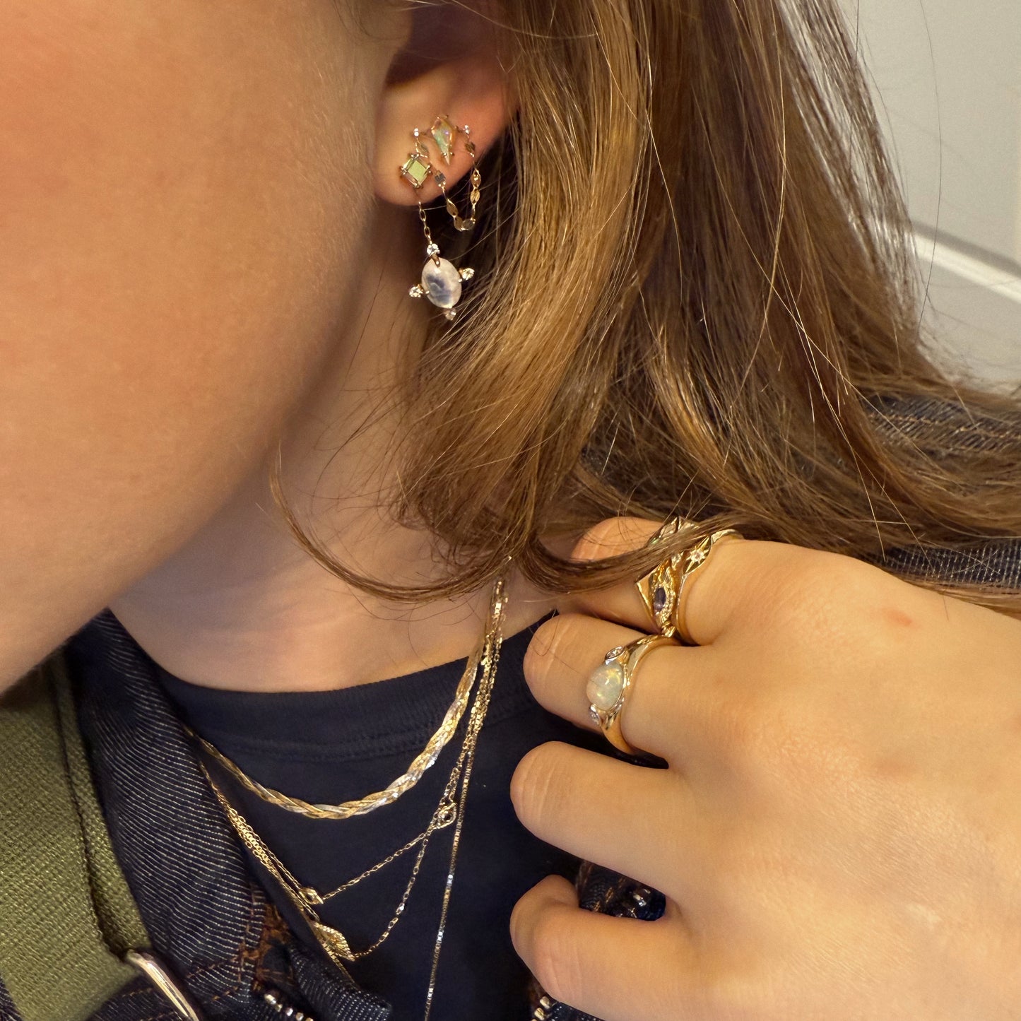 A close-up of a woman wearing layered gold necklaces, opal gold rings, and Solid Gold Crystal Ball Moonstone Drop Earrings, highlighting an elegant jewelry style.