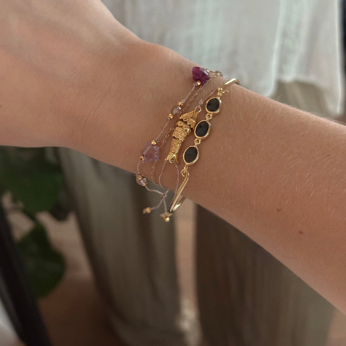 A wrist adorned with several delicate bracelets, including the Jonc Imperial Bracelet, black stone accents, and beaded strands—some from Sophie Deschamps Bijoux—shown against a softly lit background.