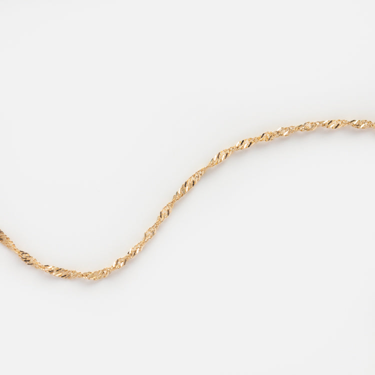The Solid Gold Twisted Chain Anklet, crafted in 9k gold, is shown against a plain white background with its delicate twisted chain gently curving across the image.