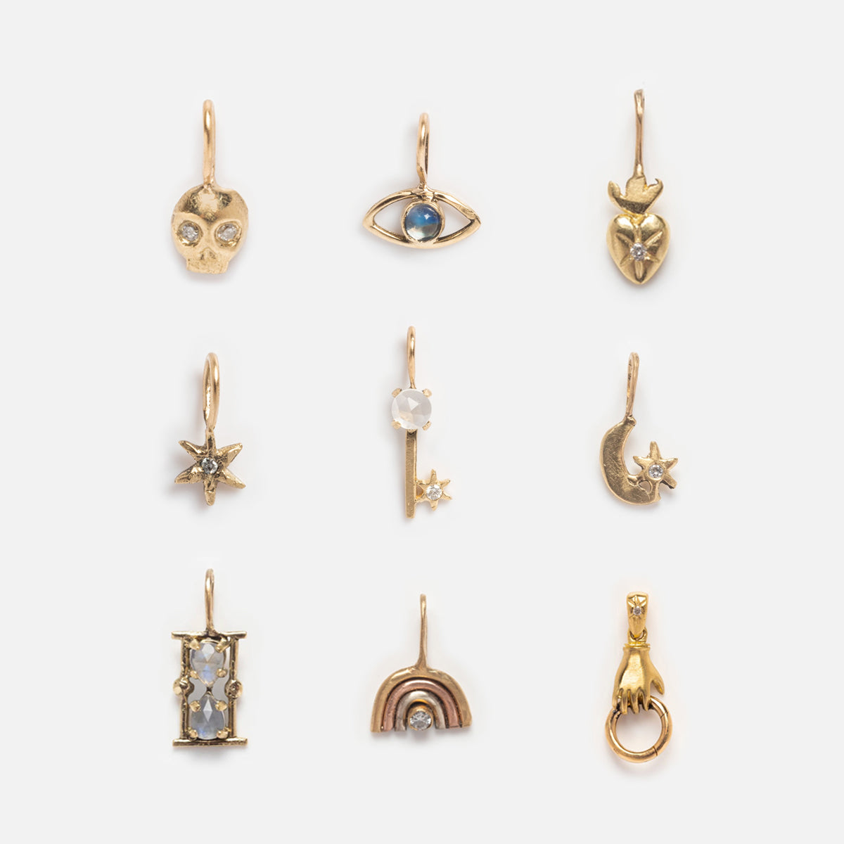 The 14k Solid Gold Tiny Charms by Acanthus feature nine unique designs—skull, eye, heart, star, bar with star, moon with star, gemstone rectangle, rainbow, and hand—each in solid yellow gold with a loop and displayed in a grid.
