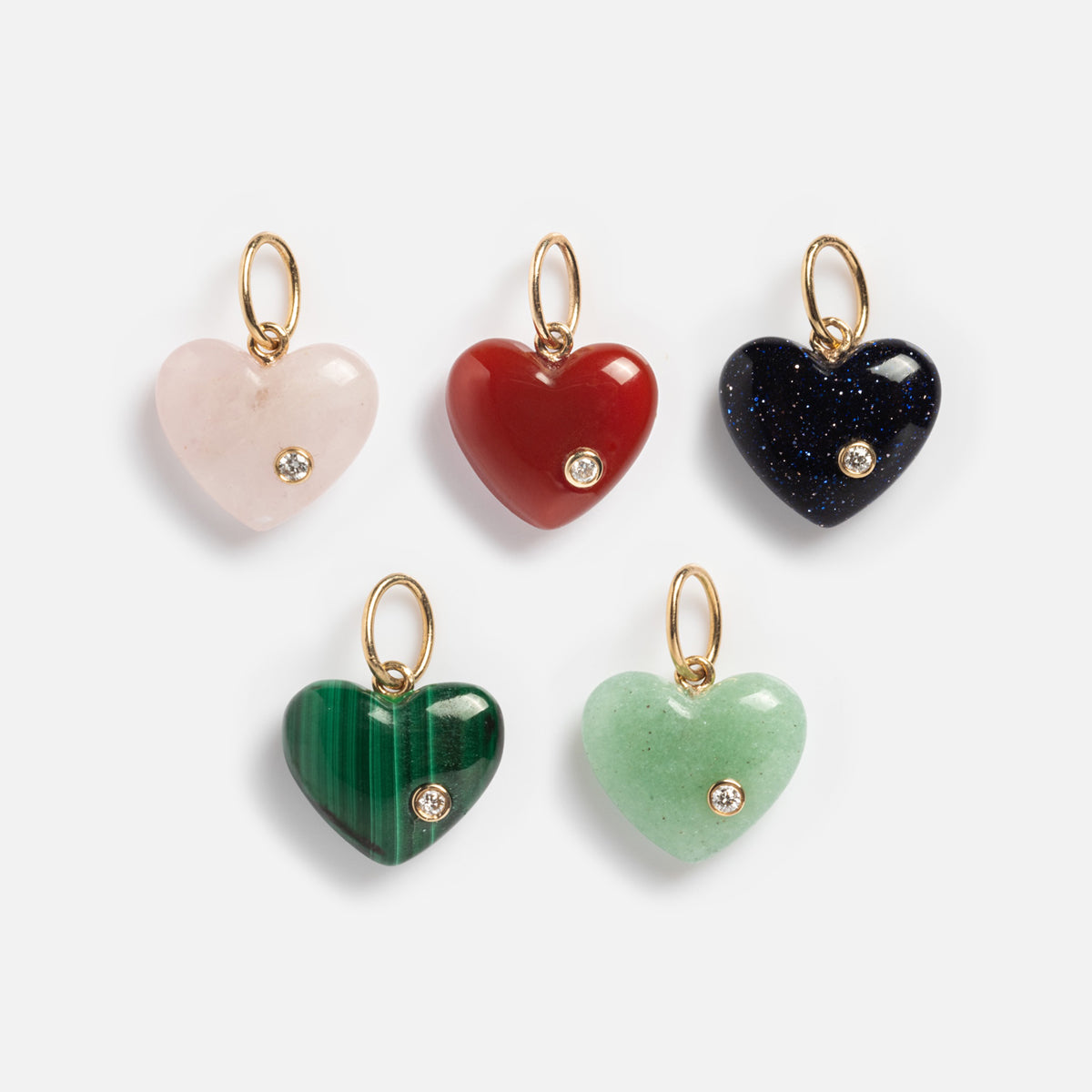 The Solid Gold Full Heart Crystal Charm comes in pink, red, dark blue, green, and light green, each featuring a small gold loop and a sparkling diamond-like crystal near the bottom right.