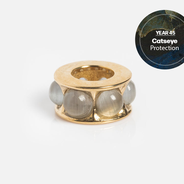 The Solid Gold Anniversaire Charm features five smooth blue-grey cat’s eye stones and an inset reading “YEAR 45 Catseye Protection” on a dark blue background—ideal for milestone jewelry lovers.