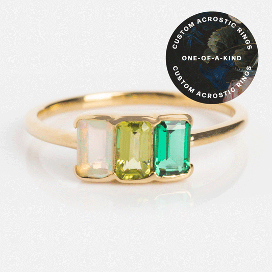 A Customizable Acrostic Baguette Gemstone Ring featuring three rectangular stones in pastel pink, light yellow-green, and vibrant green. A round sticker says: Custom Acrostic Rings, One-Of-A-Kind customizable acrostic gemstone ring.