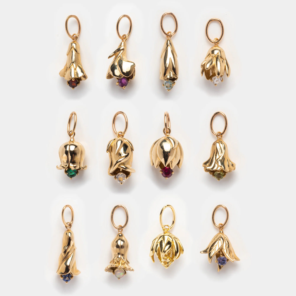 Twelve Solid Gold Birth Flower Bud Charms with colored gemstone centers are displayed in three rows. Each charm features a unique flower petal design, ideal for personalized jewelry or as a birth flower gift.