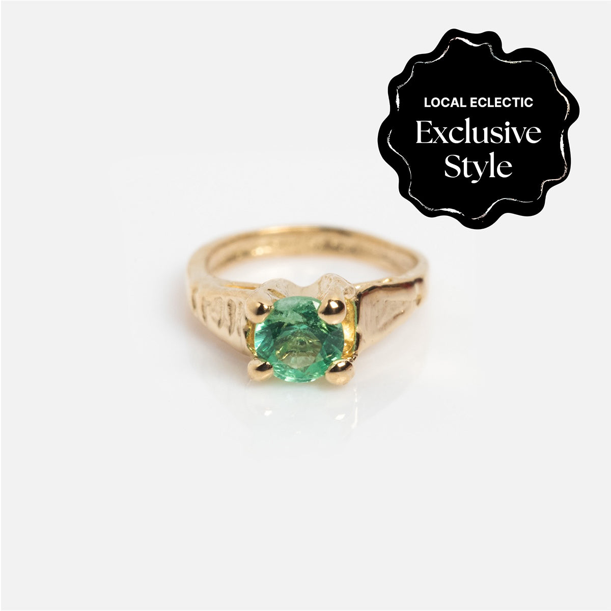 A 14k Littlest Birthstone Ring Charm with a round green gemstone sits on a white background. A black label in the top right corner reads Local Eclectic Exclusive Style, featuring Charlie and Marcelle.