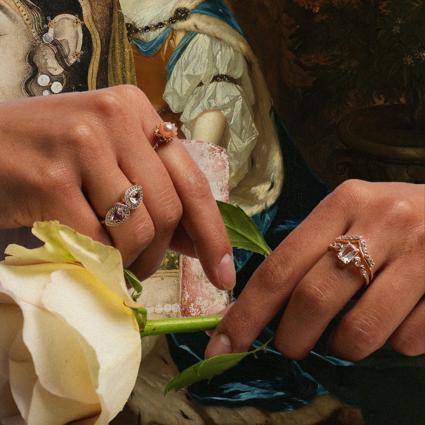 Two hands adorned with ornate rings, including the 14k Pastel Pink Pearl Statement Ring, hold a white rose. The background shows a classical painting with elaborate attire and jewelry, merging modern and historical aesthetics.