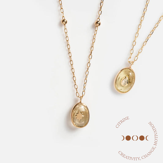 Two Solid Gold Crystal Amulet Necklaces for Manifestation, each with an oval citrine pendant—one adorned with a star. Nearby is a circular text: CITRINE, CREATIVITY, CHANGE, MOTIVATION and moon phases. The perfect necklace for manifestation.