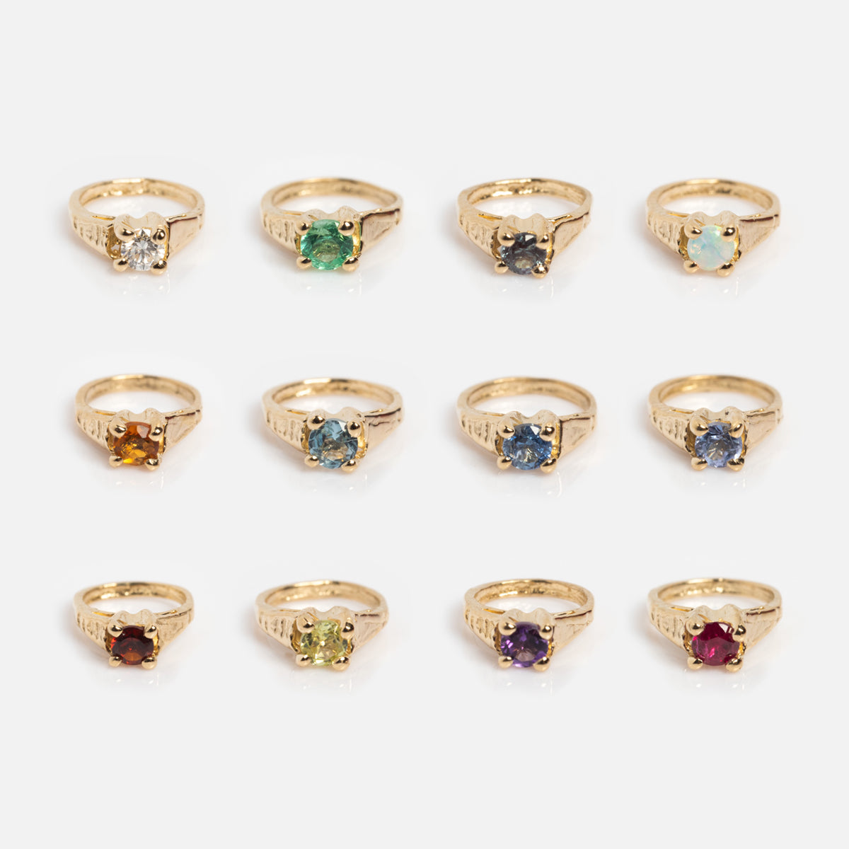 Twelve 14k Littlest Birthstone Ring Charms, each with a unique gemstone—clear, green, blue, opal, orange, light blue, yellow, purple, and red—are arranged in rows. Perfect for your Charlie and Marcelle solid gold necklace.