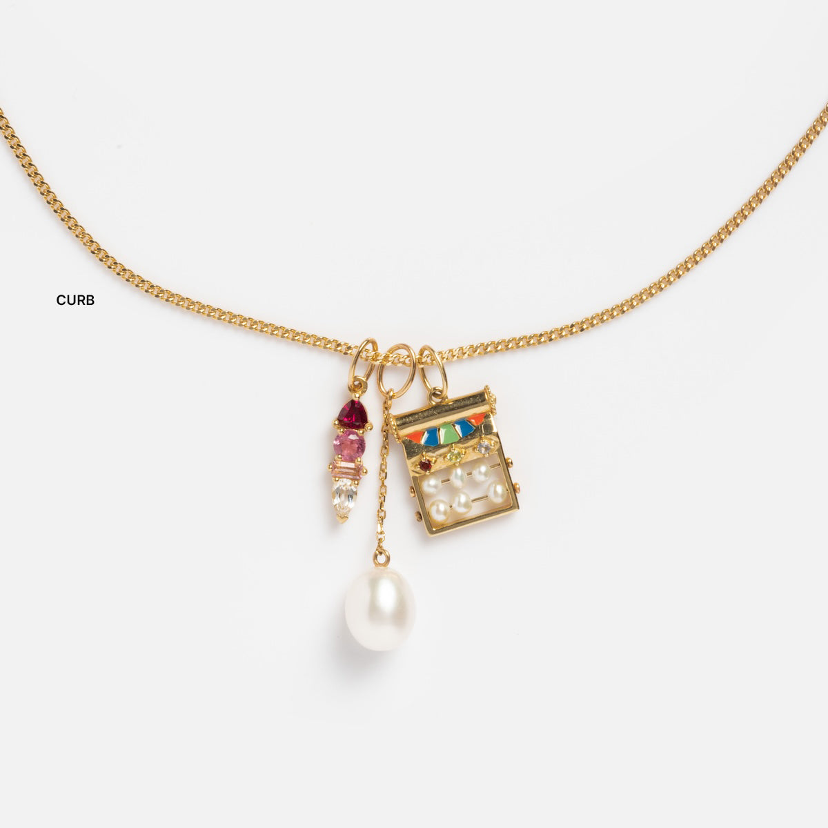 The Solid Gold Chain for Charms features a curb chain with three unique charms—a pearl drop, a gold-framed pendant with pearls and colorful stones, and a cluster of a red stone and clear beads—displayed on a white background.