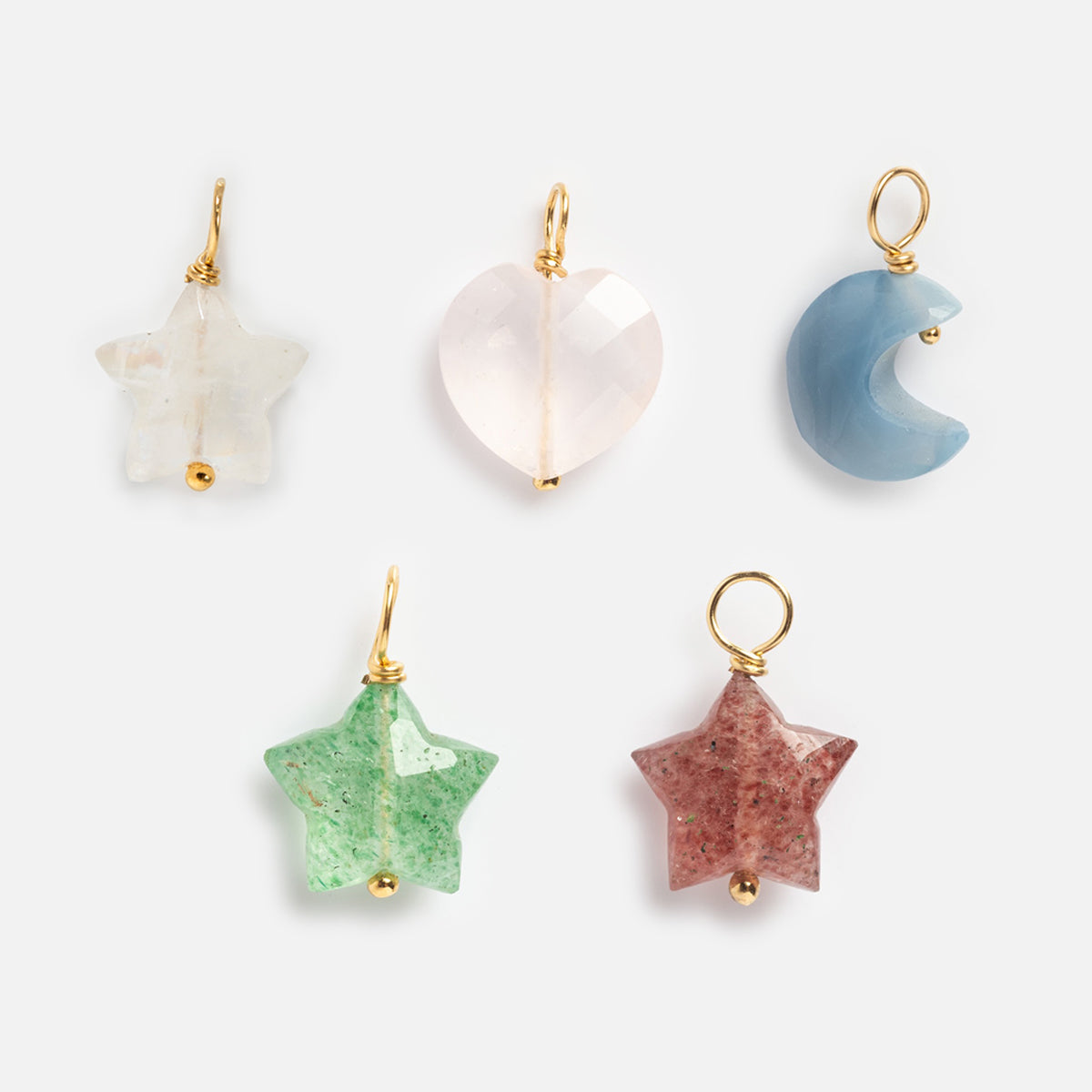 Five Devi Arts Collective x Local Eclectic Carved Crystal Charms—two star (white, green), one heart (pink), one crescent moon (blue), and one red star—each with gold loops, are displayed on a light gray background.