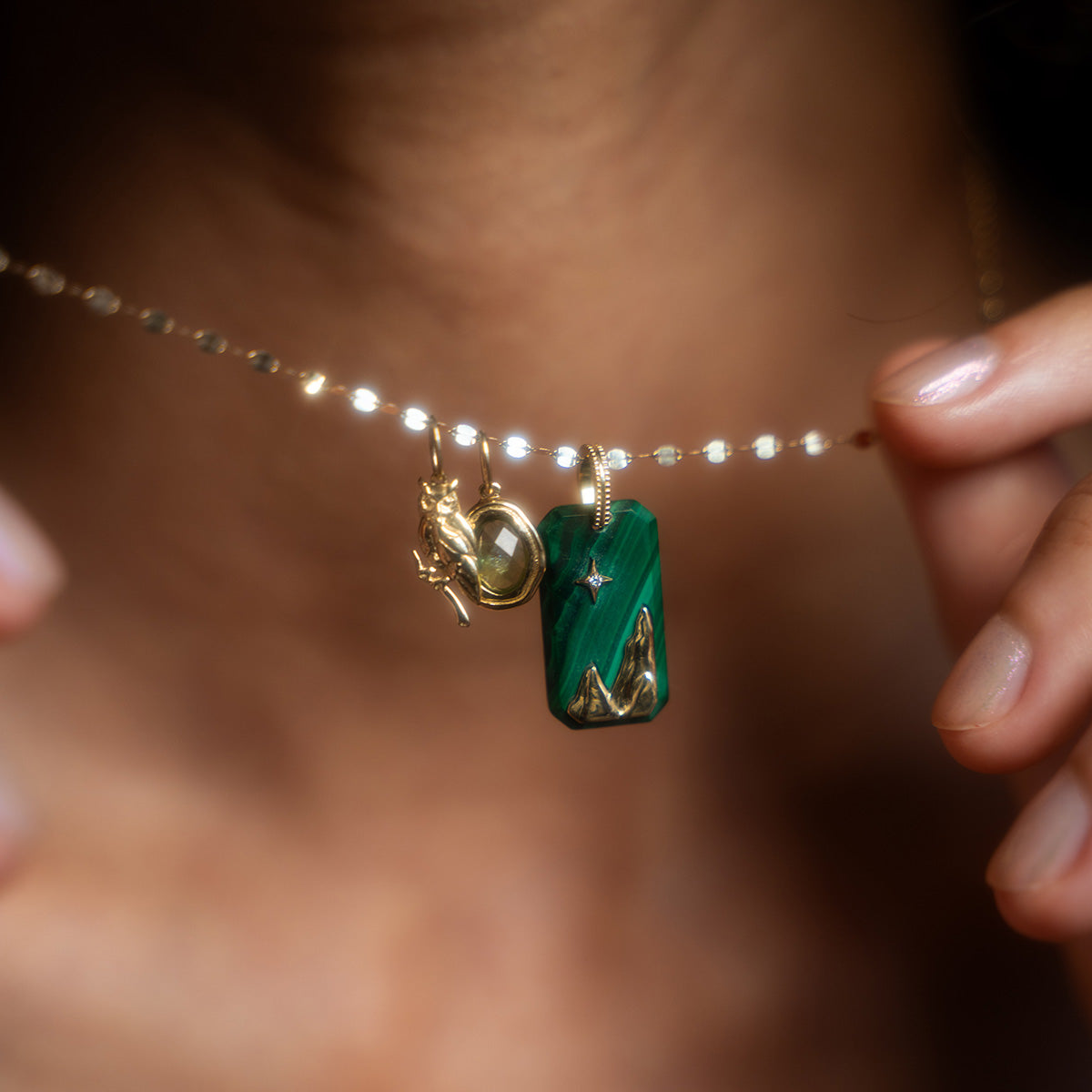 A person holding a Solid Gold Crystal Element Charm necklace with a natural crystal pendant.