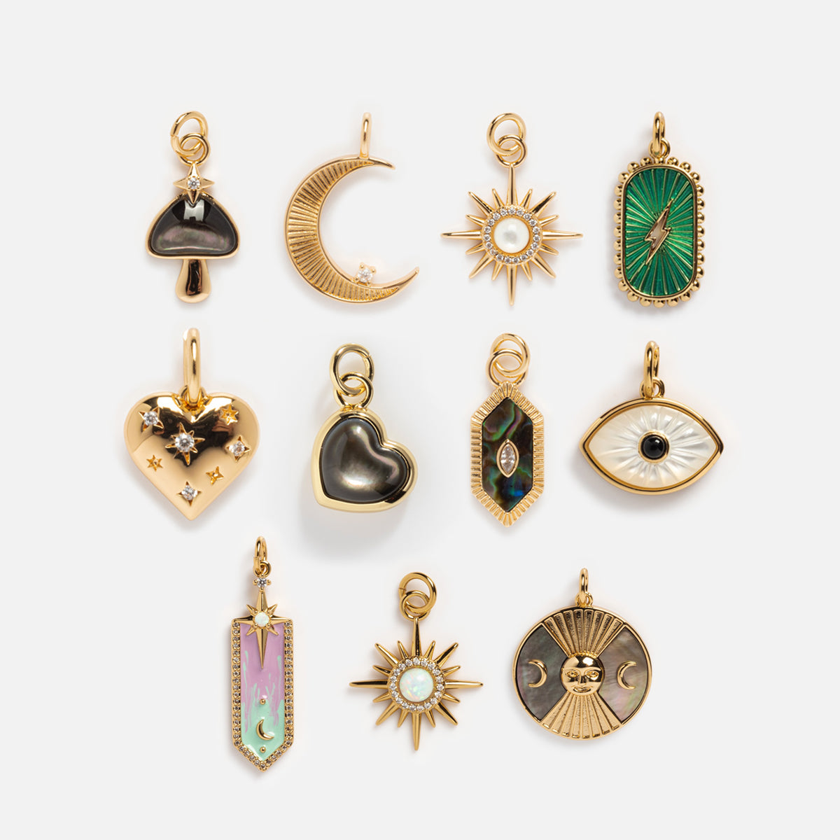 Charms by Elizabeth Stone: Set of 11 celestial 14k gold plated charms in crescent moon, stars, heart, eye, sunburst, and geometric shapes. Features colorful enamel, mother of pearl accents, gemstones on a white background.