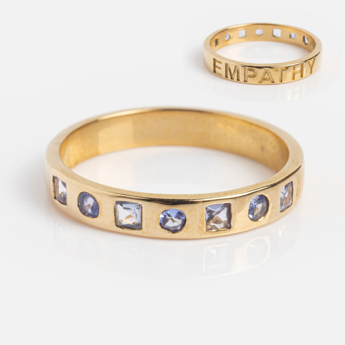 The Solid Gold Within You Birthstone Band Sample Size 7 features two 9k yellow gold rings: one with six square natural stones, the other plain engraved “EMPATHY.” Both have a 3.1mm band width and are shown on a white background.