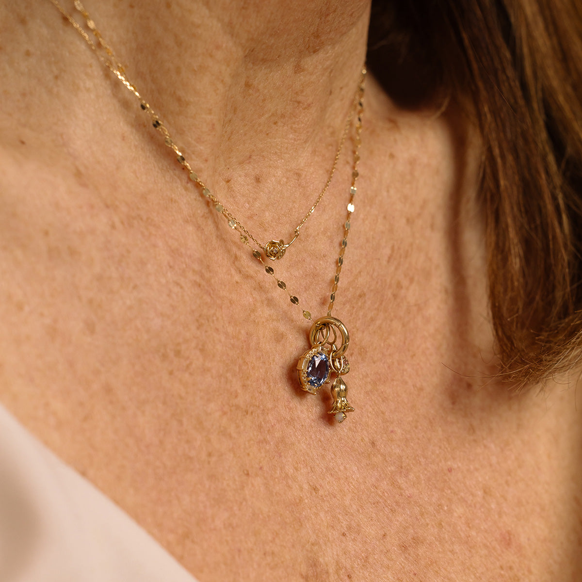 A close-up of a womans neck wearing the Solid Gold Birth Flower Necklace, featuring delicate solid gold with three pendants—a purple birthstone, a flower-shaped charm, and a small charm—for an elegant jewelry look.