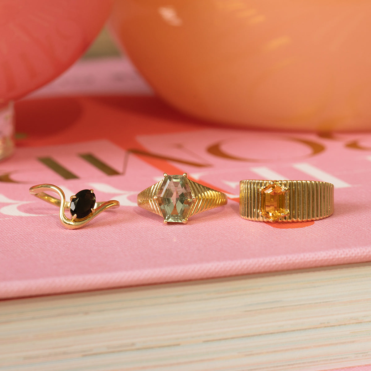 The Solid Gold Green Amethyst Bold Chevron Ring, crafted from 9k yellow gold, is shown atop a pink book with its pages fanned below.