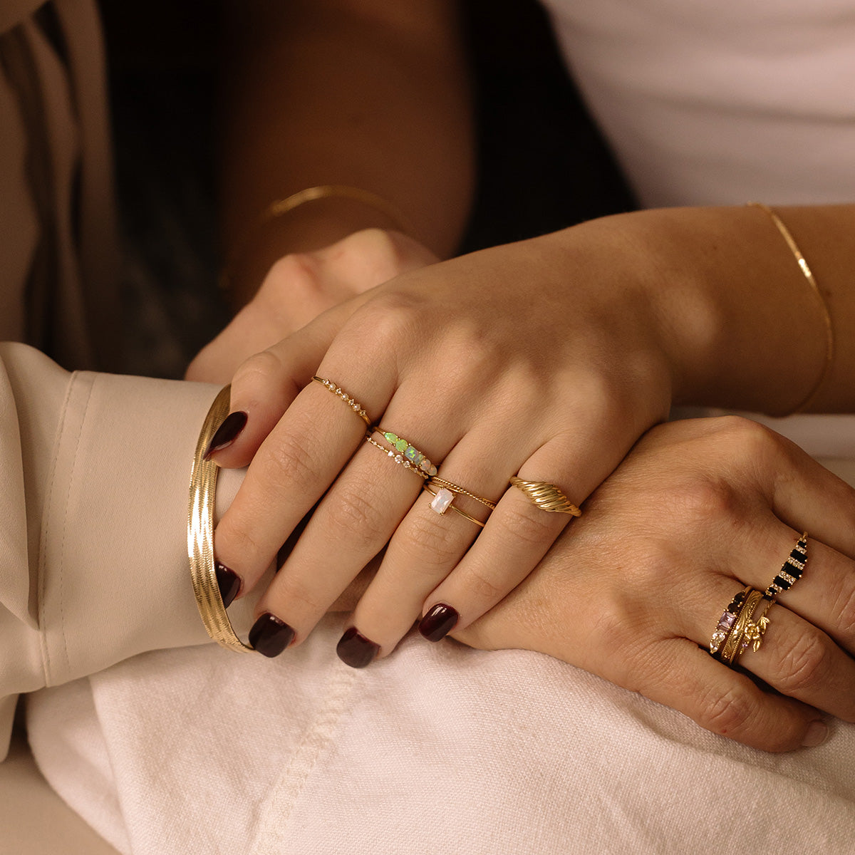 Two hands with manicured nails, each wearing the Solid Gold Crossover Ring Set by Local Eclectic, rest gently atop one another to showcase these elegant rings against a soft, neutral background.