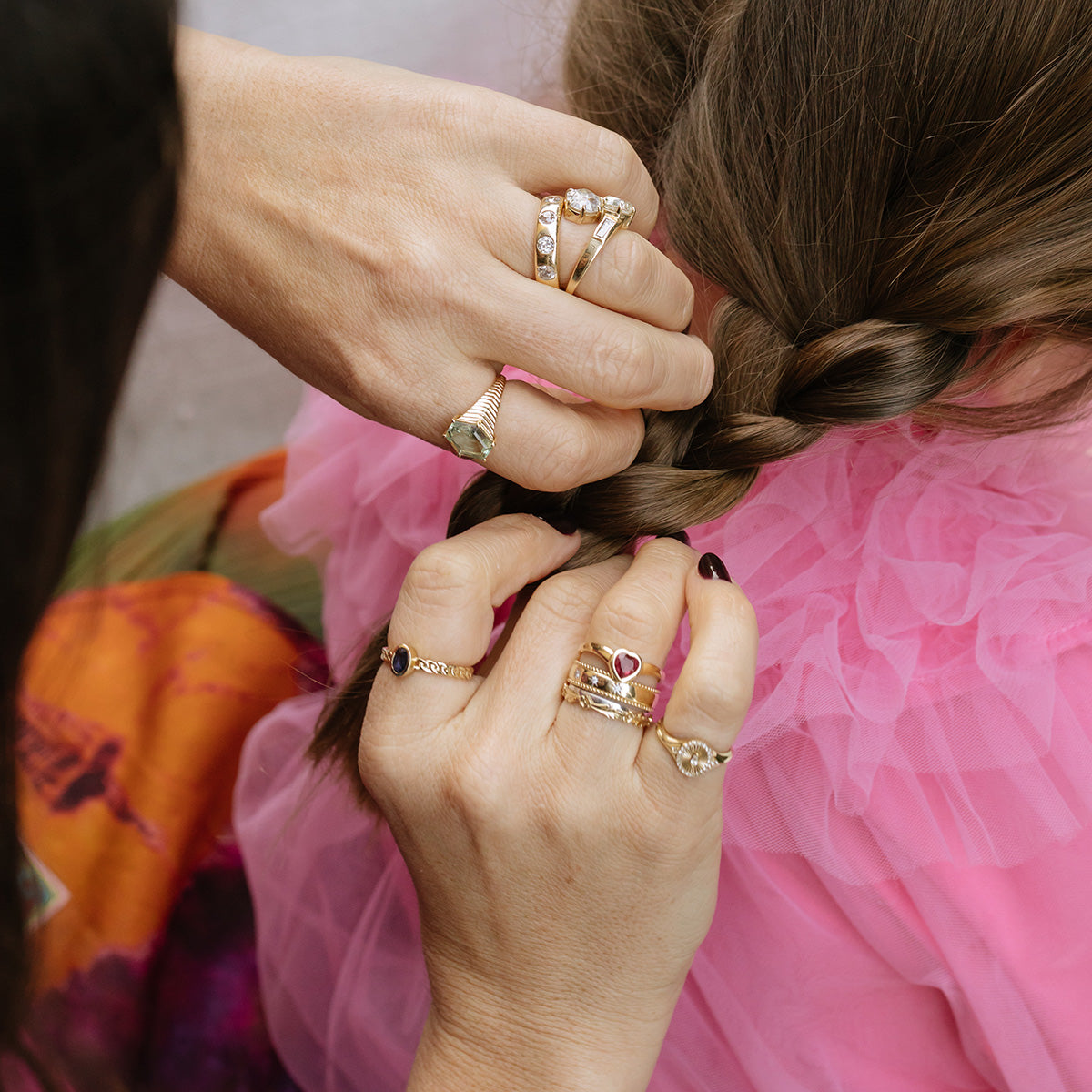 Close-up of two hands wearing the Solid Gold Bold Star Set Diamond Band braiding a young girl’s brown hair; the girl is dressed in a pink ruffled top.