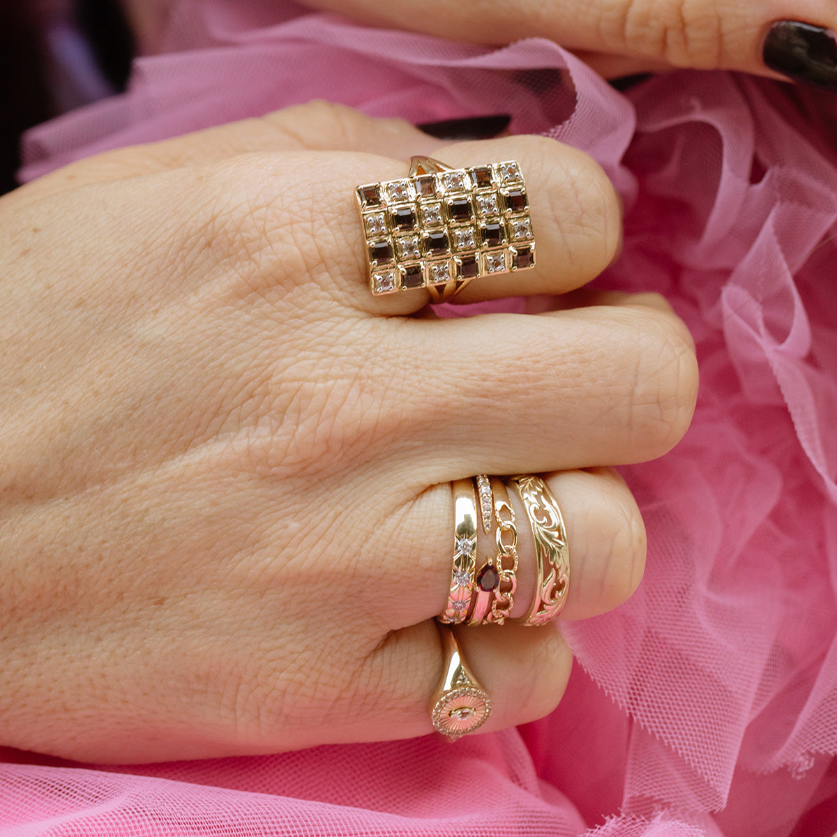 A close-up of a hand wearing the Solid Gold Vintage Inspired Diamond Band, along with other gold rings, rests against pink ruffled fabric.