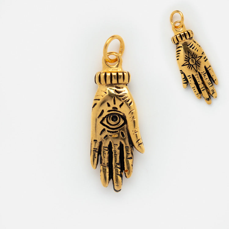 Charms by Hunt of Hounds: a set of two gold vermeil hand-shaped charms, one with an engraved eye and the other with a sunburst, both featuring ornate detailing and a loop for hanging.