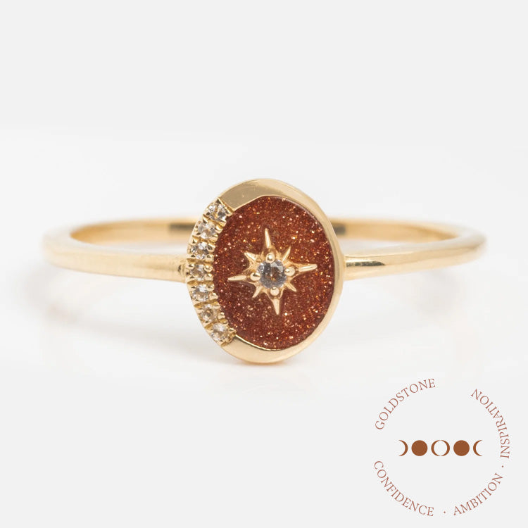 The Solid Gold Crystal Crescent Moon Ring for Manifestation features a crescent moon design with a sparkling centerpiece. Displayed on a white background with “Goldstone, Confidence, Ambition, Inspiration” in circular text.