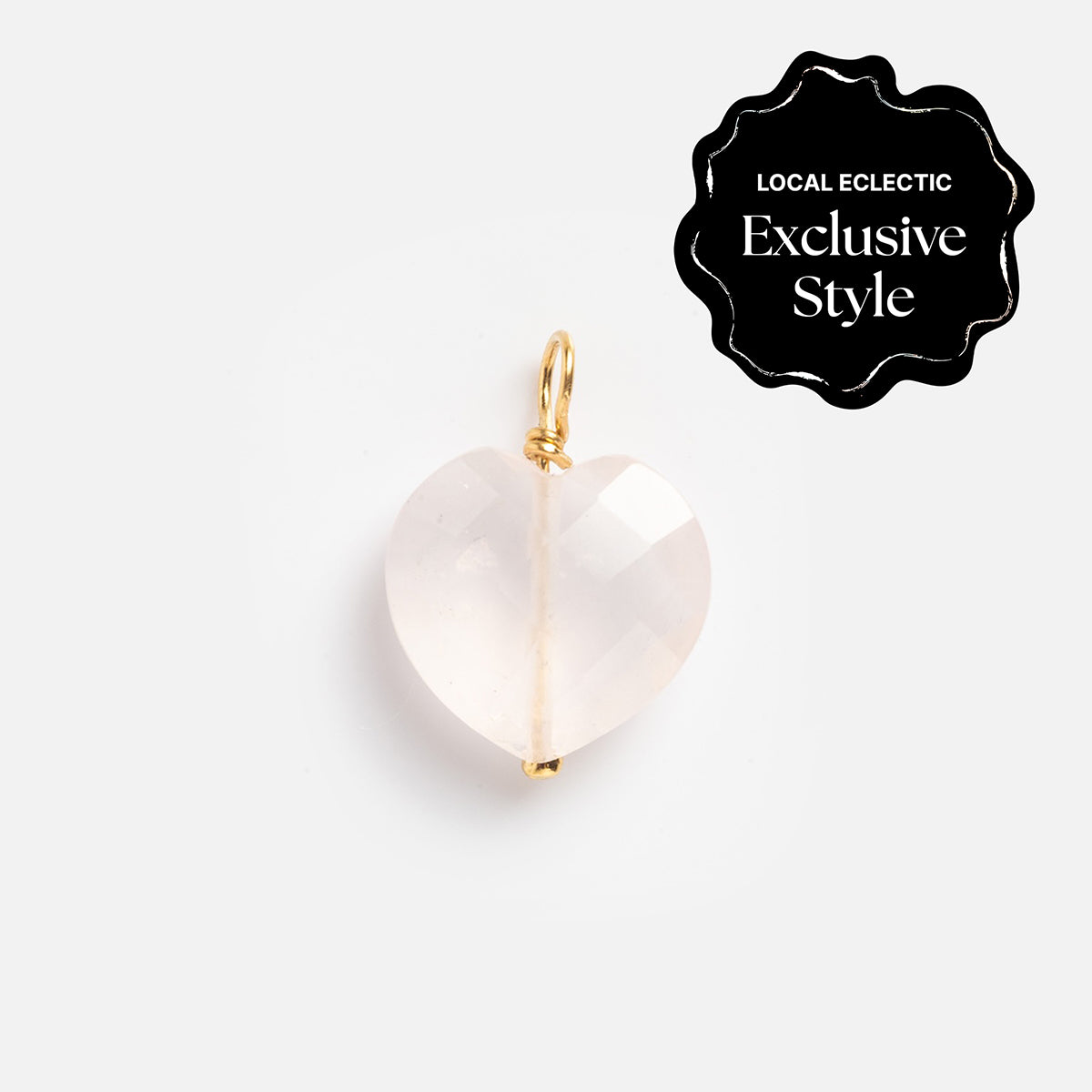 A faceted, heart-shaped rose quartz charm with a gold loop is set on a white background. A black badge in the corner reads: Devi Arts Collective x Local Eclectic Carved Crystal Charms—exclusive for crystal and gemstone jewelry lovers.