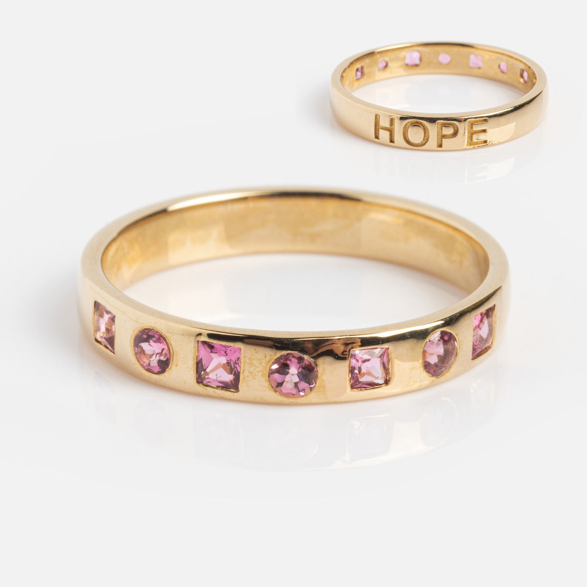 The Solid Gold Within You Birthstone Band (Sample Size 7) is a 9k yellow gold ring with a 3.1mm band featuring alternating square and round pink gemstones set along the band.