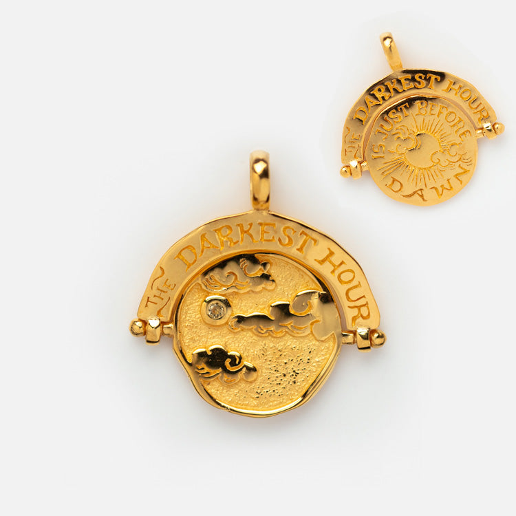 Charms by Hunt of Hounds: a gold vermeil pendant engraved with a night sky and clouds, THE DARKEST HOUR above. The reverse shows a sun and reads IS JUST BEFORE THE DAWN.
