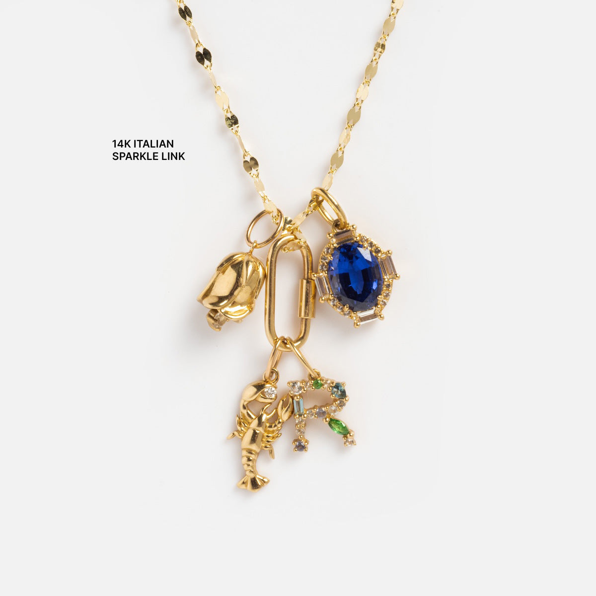 A Solid Gold Chain for Charms featuring four charms: a small shell, a blue gemstone in gold, a lobster, and a leafy branch with green and clear stones. Text reads 14K ITALIAN SPARKLE LINK.