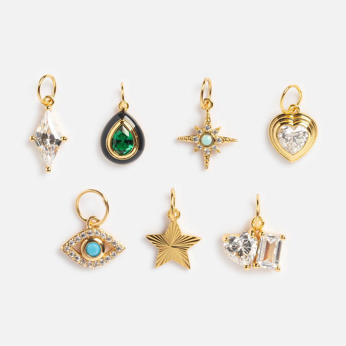 Seven small yellow gold-plated Charms by Jurate JLA, each with gem-focused designs—diamond, teardrop, heart, eye, and stars—featuring colorful stones and crystal embellishments, are beautifully arranged on a white background.