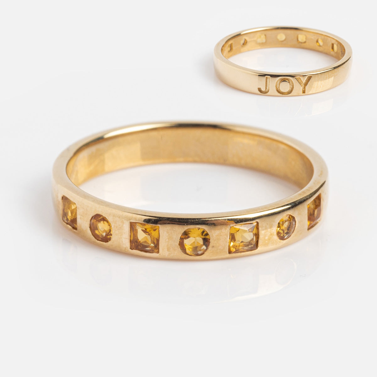 The Solid Gold Within You Birthstone Band (sample size 7) is a 9k yellow gold ring with JOY engraved inside and seven natural stones set along its 3.1 mm band, displayed on a white background.