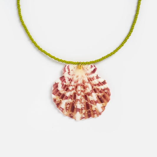 The Rincon Necklace, featuring a green seed bead chain and a large pink-and-white patterned seashell pendant, is displayed against a plain white background.
