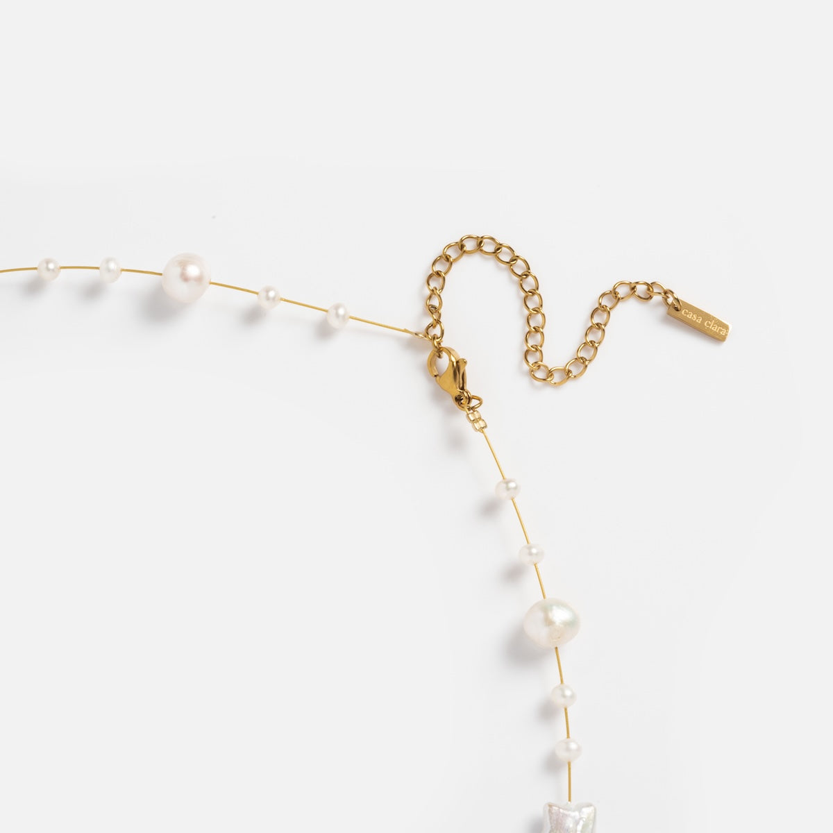 The Suki Necklace is gold plated, features natural pearls in various sizes, a lobster clasp with adjustable extender chain, and a small rectangular gold tag, shown on a white background.