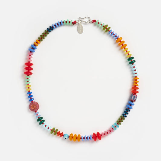 The Rainbow Candy Necklace features handmade glass beads in red, blue, green, yellow, and orange with a pink flower-shaped bead and a silver clasp—perfect for fans of playful, colorful jewelry.
