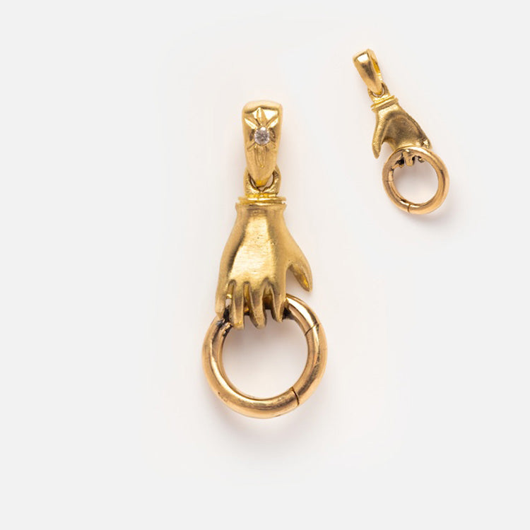 Two 14k solid gold hand-shaped charms by Acanthus, each grasping a ring; the larger features a star detail on the wrist. Both are shown against a plain white background.